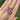Kunzite gemstone and diamond ring on a hand with a blurred green outdoor background