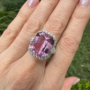 Kunzite  gemstone and diamond ring on a hand with a blurred green outdoor background