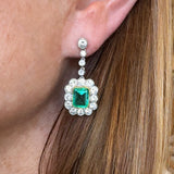 Close-up of an earring with a emerald and diamonds worn by a person.