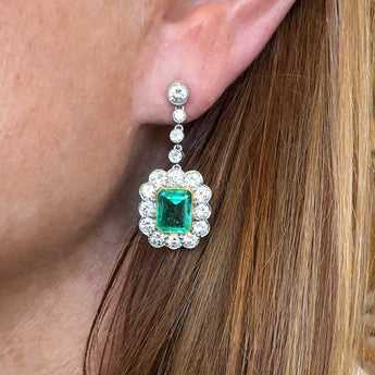 Close-up of an earring with a emerald and diamonds worn by a person.